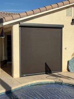 Black drop shades enclosing a poolside outdoor kitchen